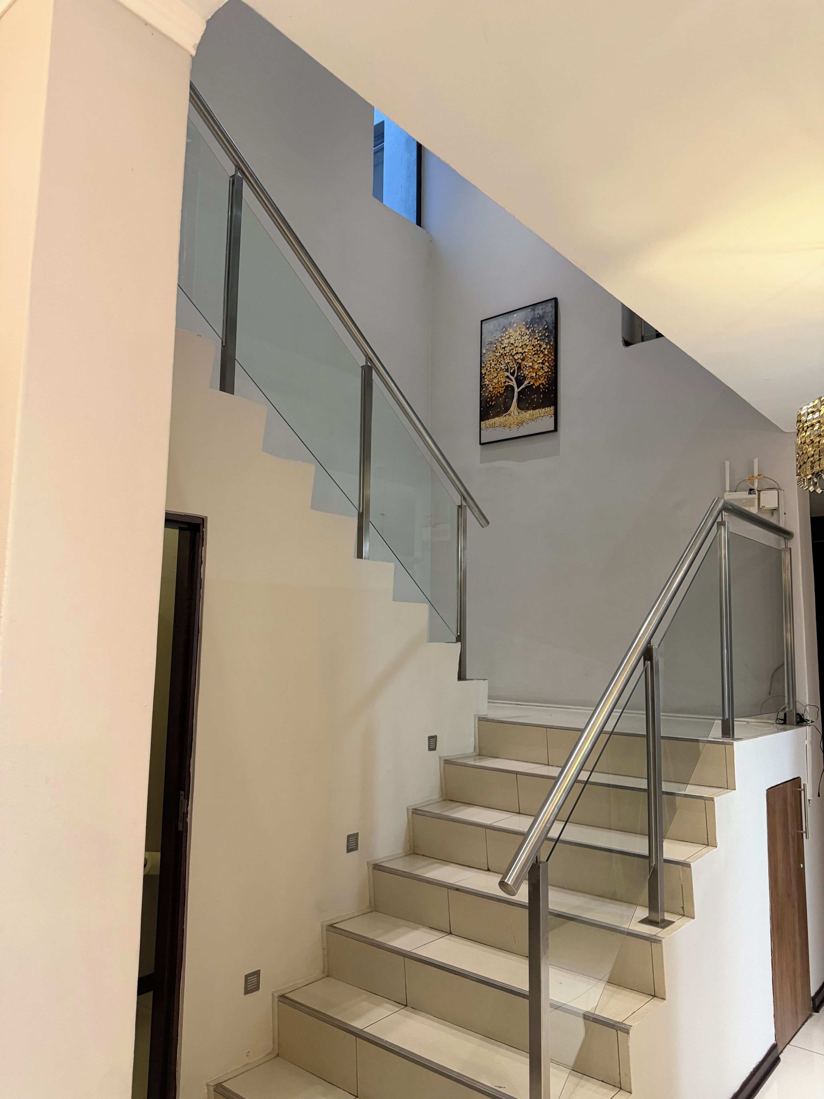 Un escalier moderne avec des rampes en verre et un tableau représentant un arbre.