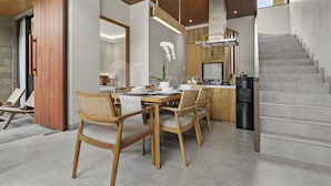 Cozinha moderna com fogão embutido, área de jantar com cadeiras de madeira e uma mesa, e escada que leva a um andar superior.