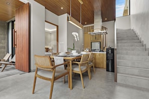 A modern kitchen with a built-in stove, a dining area with wooden chairs and a table, and a staircase leading to an upper level. - Bel Air Villa by Kozystay - Canggu (Badung)