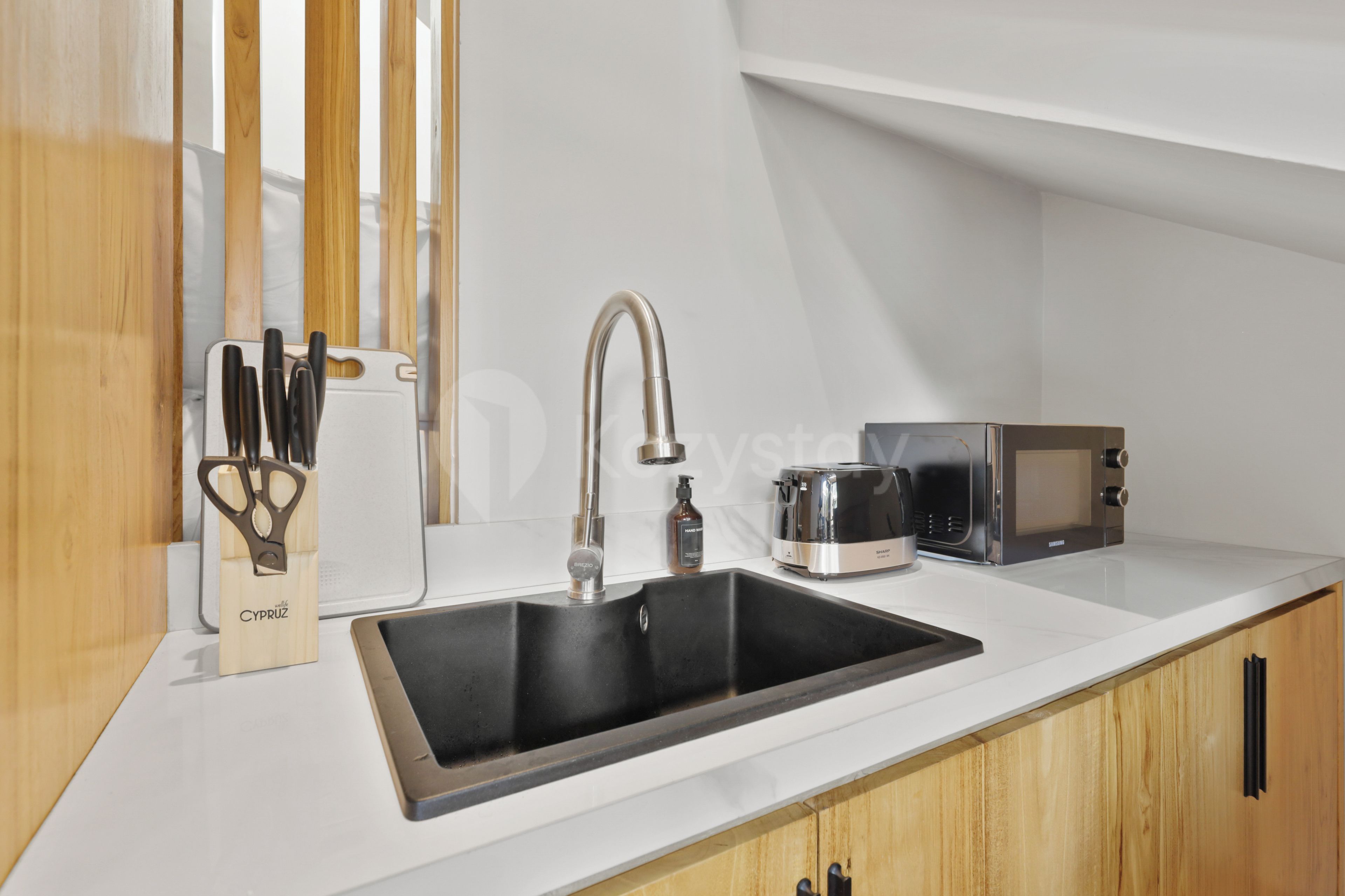 A modern kitchen with a black sink, stainless steel appliances, and wooden cabinetry.