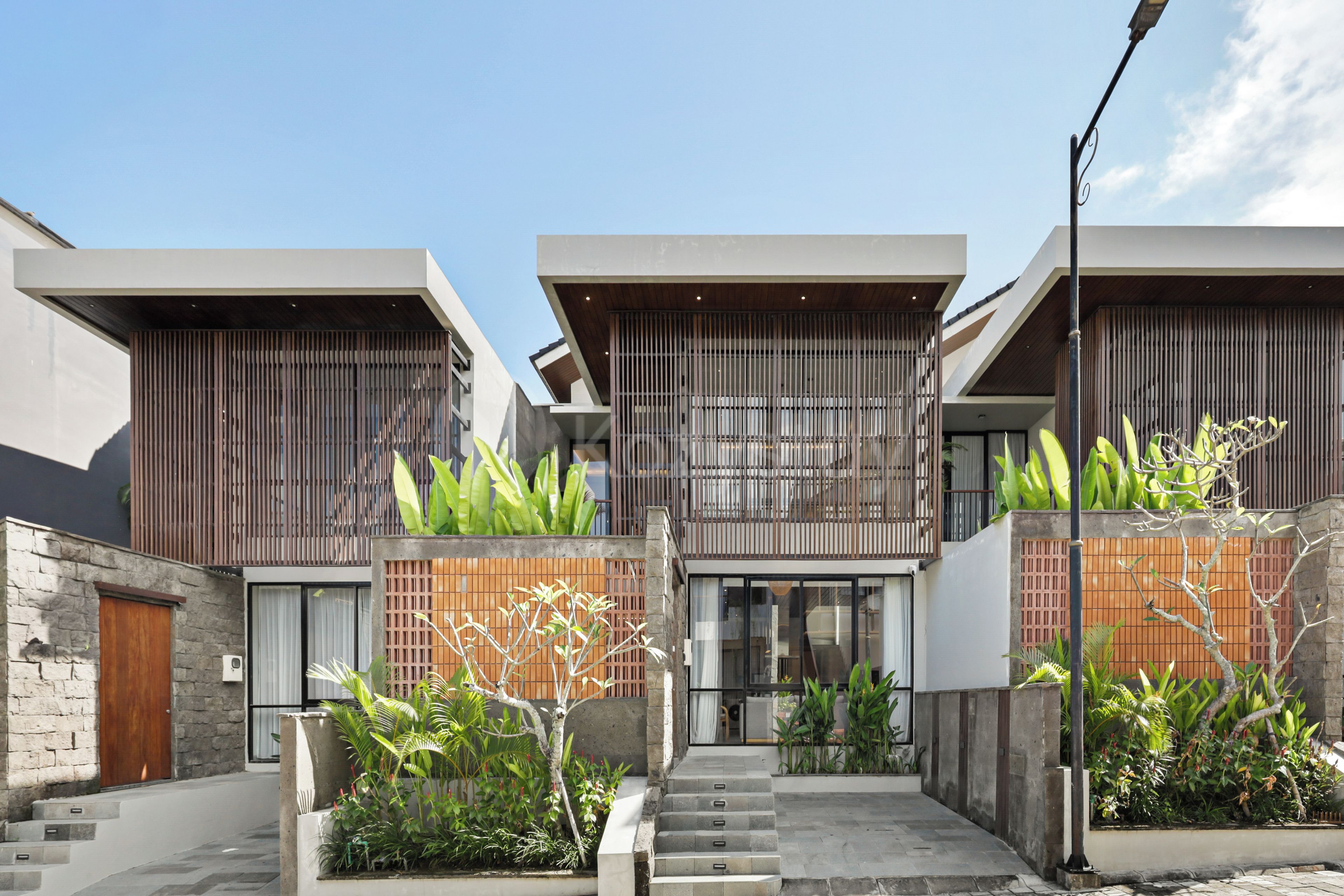 A modern residential building with a central courtyard, featuring a staircase leading to the entrance, surrounded by lush greenery and a mix of wooden and stone materials.