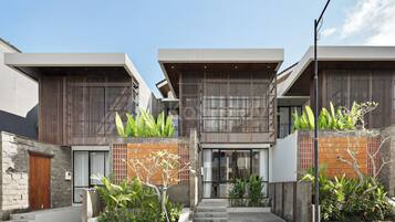 A modern residential building with a central courtyard, featuring a staircase leading to the entrance, surrounded by lush greenery and a mix of wooden and stone materials.