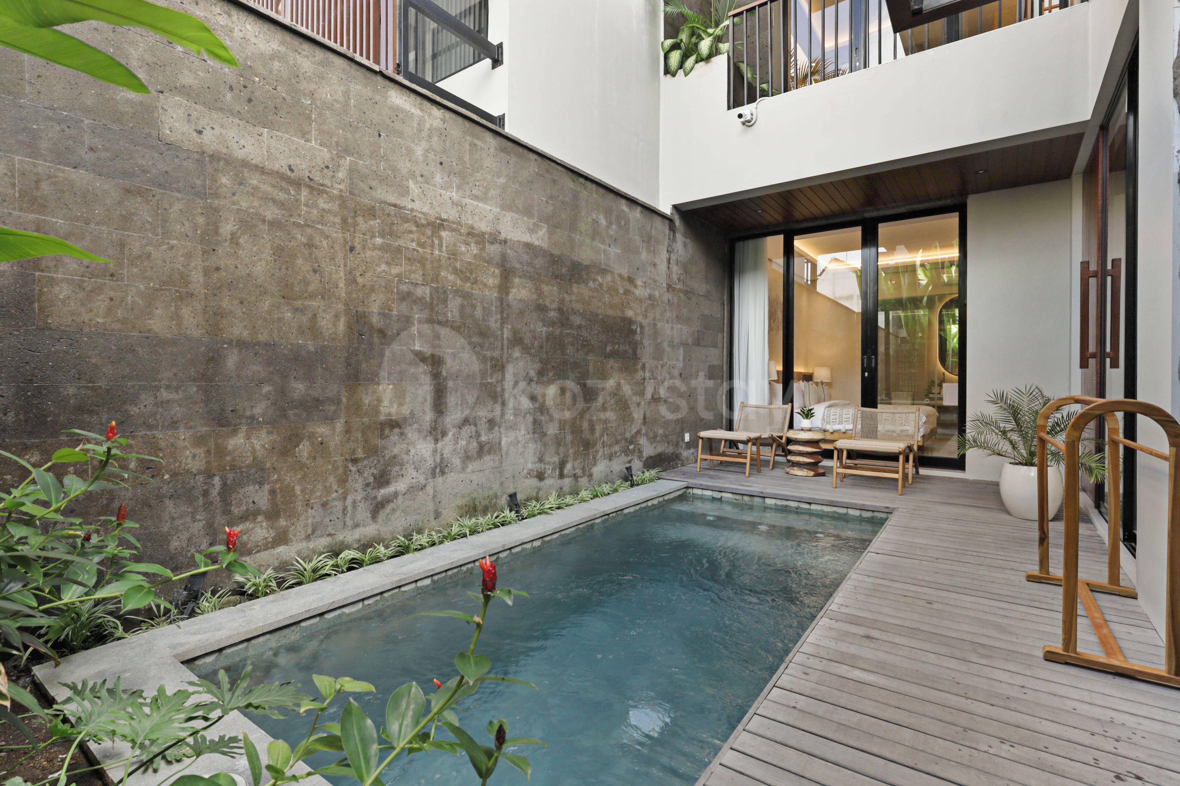 A modern outdoor pool area with a concrete wall, wooden deck, and lounge chairs.
