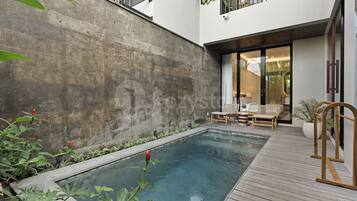 A modern outdoor pool area with a concrete wall, wooden deck, and lounge chairs.