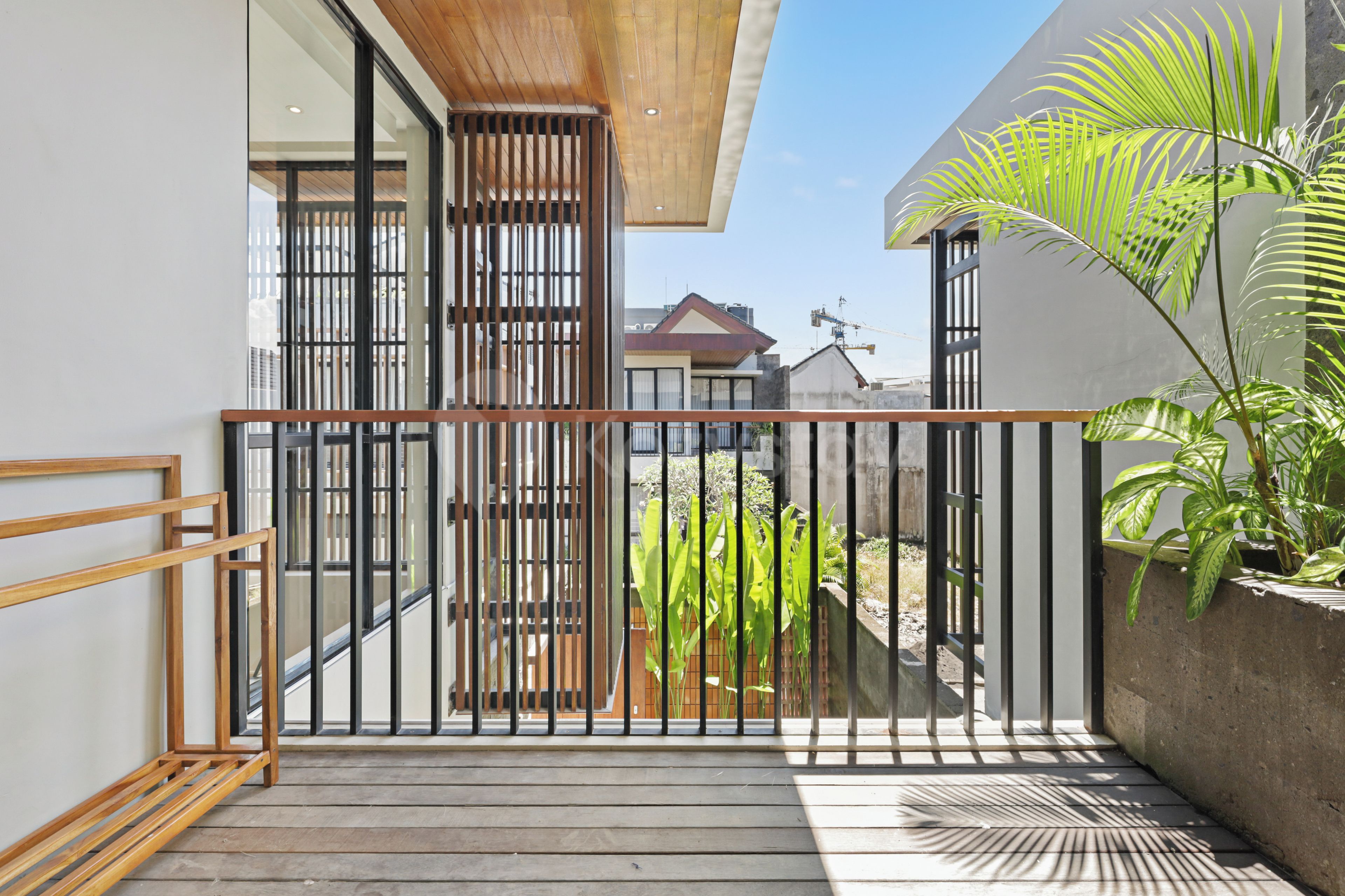 Un balcón moderno con piso de madera, barandilla de metal y vista a una zona residencial.
