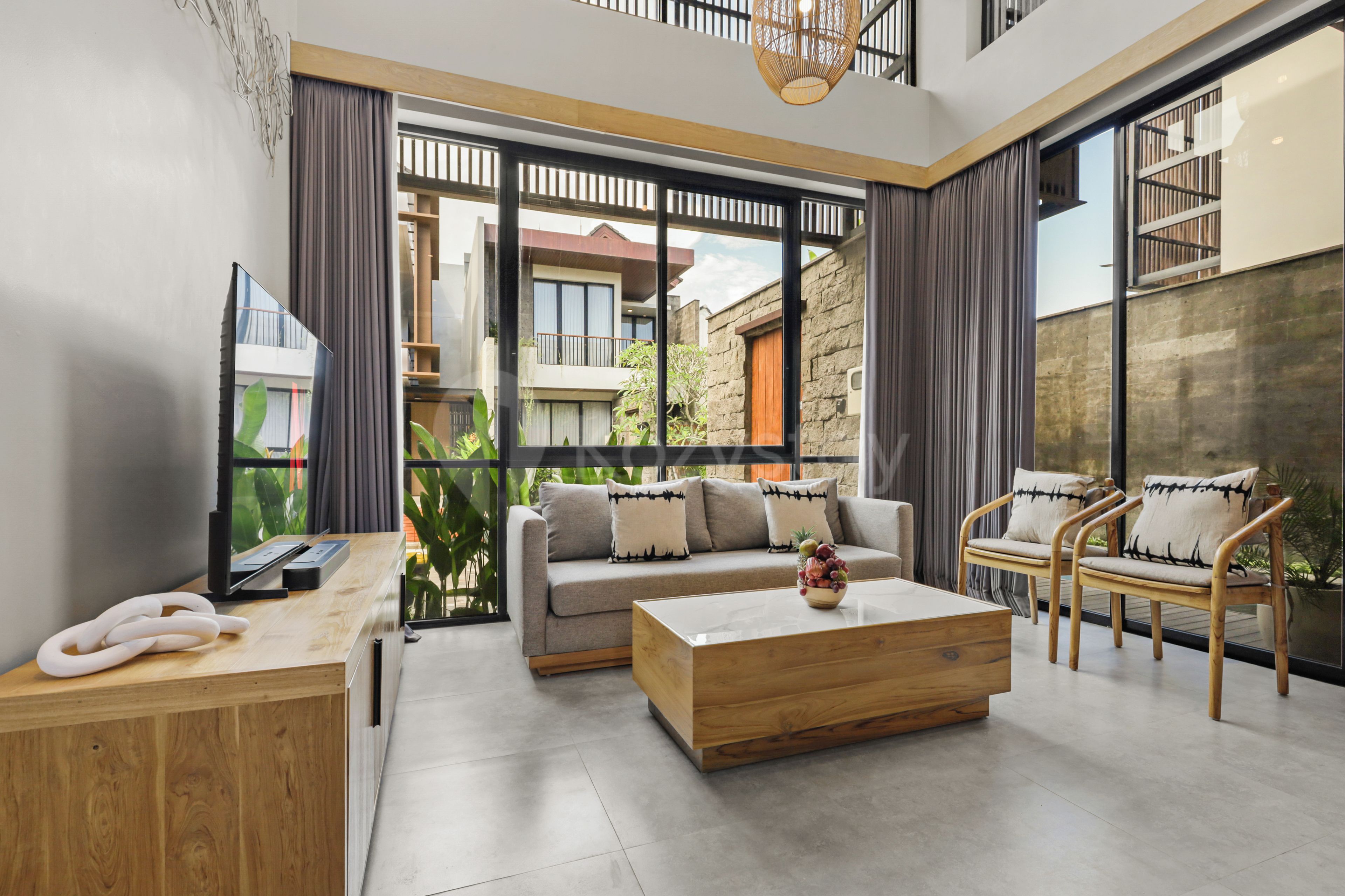 A modern living room with a sofa, coffee table, and chairs, large windows, and a view of the outside.