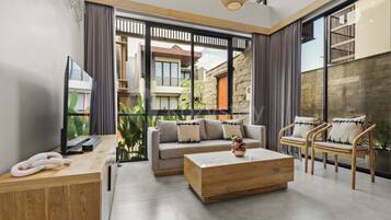 A modern living room with a sofa, coffee table, and chairs, large windows, and a view of the outside.