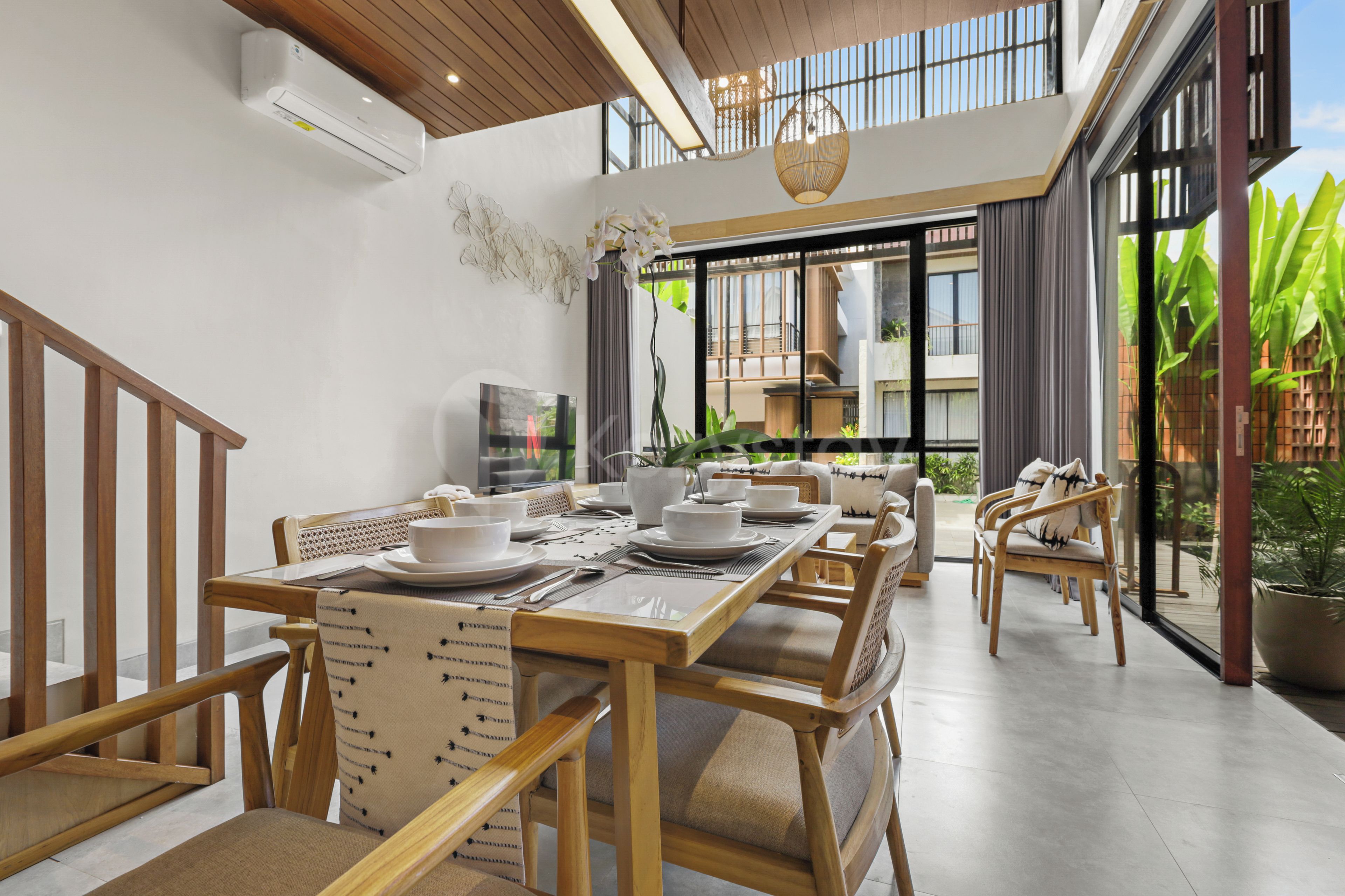 A dining area with a wooden table set for four, surrounded by chairs, and a television on the wall.