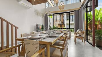 A dining area with a wooden table set for four, surrounded by chairs, and a television on the wall.