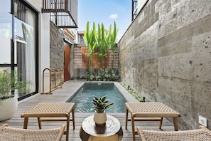 A modern outdoor pool area with two wicker chairs and a small table, surrounded by plants and a concrete wall. - Bel Air Villa by Kozystay - Canggu (Badung)