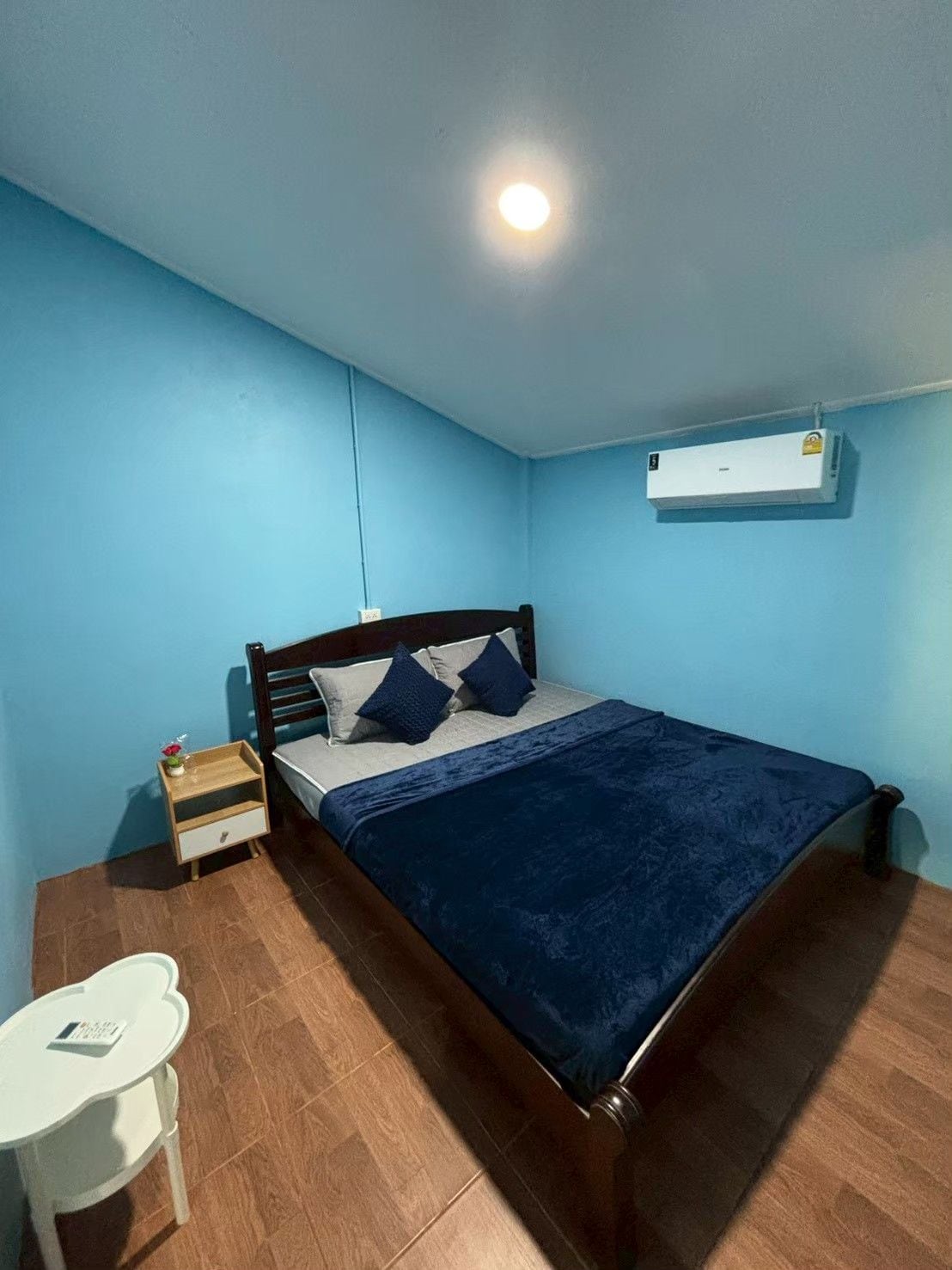 Un dormitorio con cama, mesita de noche, una pequeña mesa y un equipo de aire acondicionado en la pared.