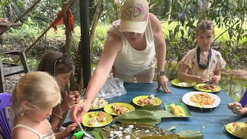 Un groupe de personnes est assis à une table à l’extérieur, avec de la nourriture et des couverts devant elles.