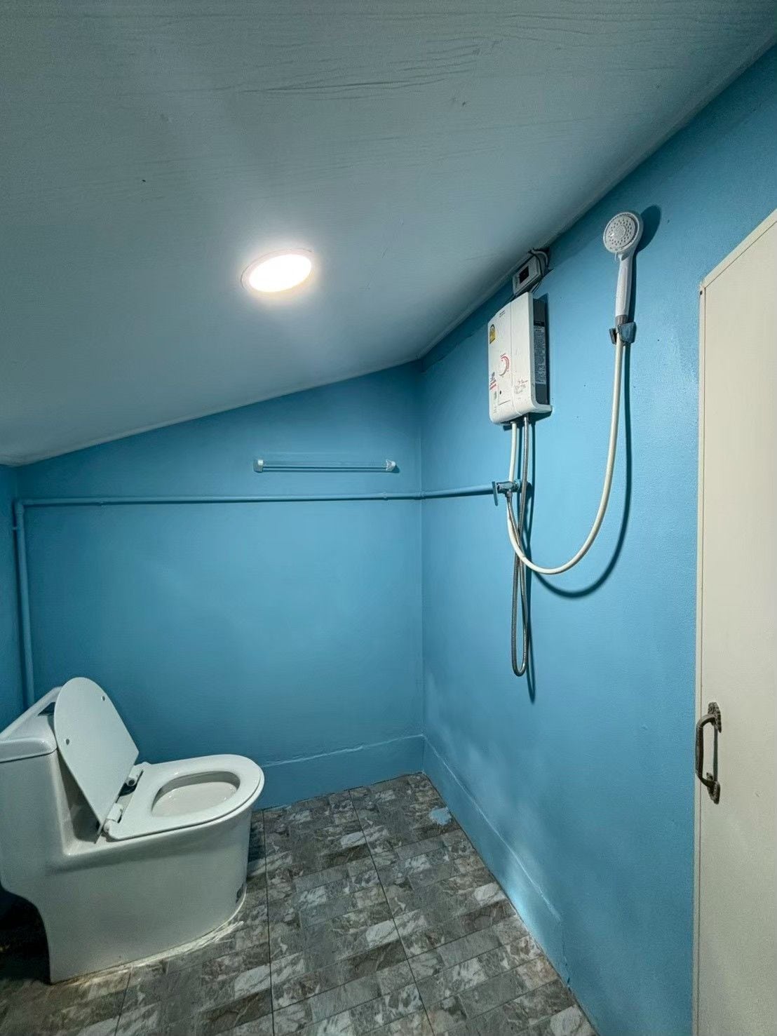 Un baño pequeño y cerrado con inodoro, cabina de ducha y calentador de pared.