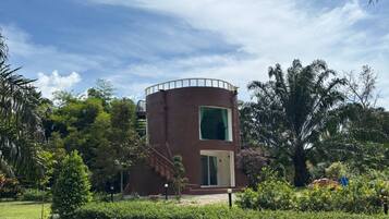 Un edificio circular con techo plano, rodeado de un jardín bien cuidado con arbustos y árboles variados.
