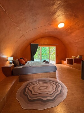 A cozy, curved room with a bed, a nightstand, a lamp, and a view of greenery outside. - khaosoksaengtawanresortandcamp (Phanom)