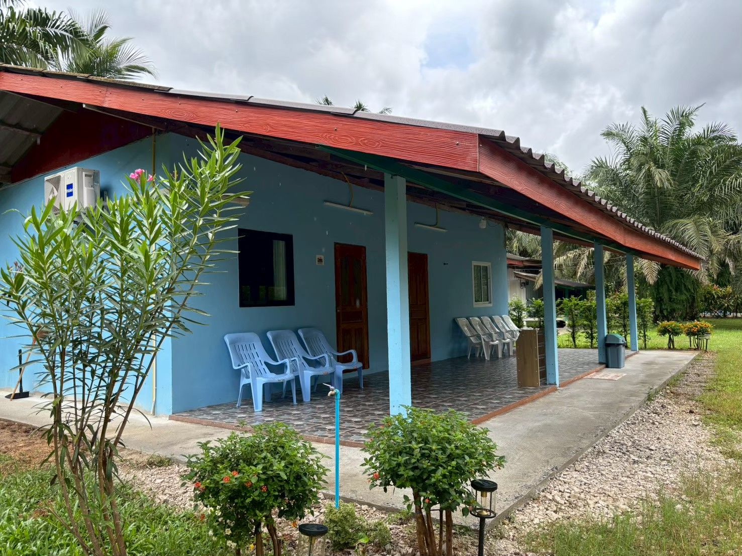 A blue building with a red roof, a covered porch, and several white plastic chairs.