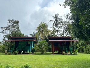 Two small, single-story buildings with green staircases, surrounded by lush greenery and palm trees. - khaosoksaengtawanresortandcamp (Phanom)