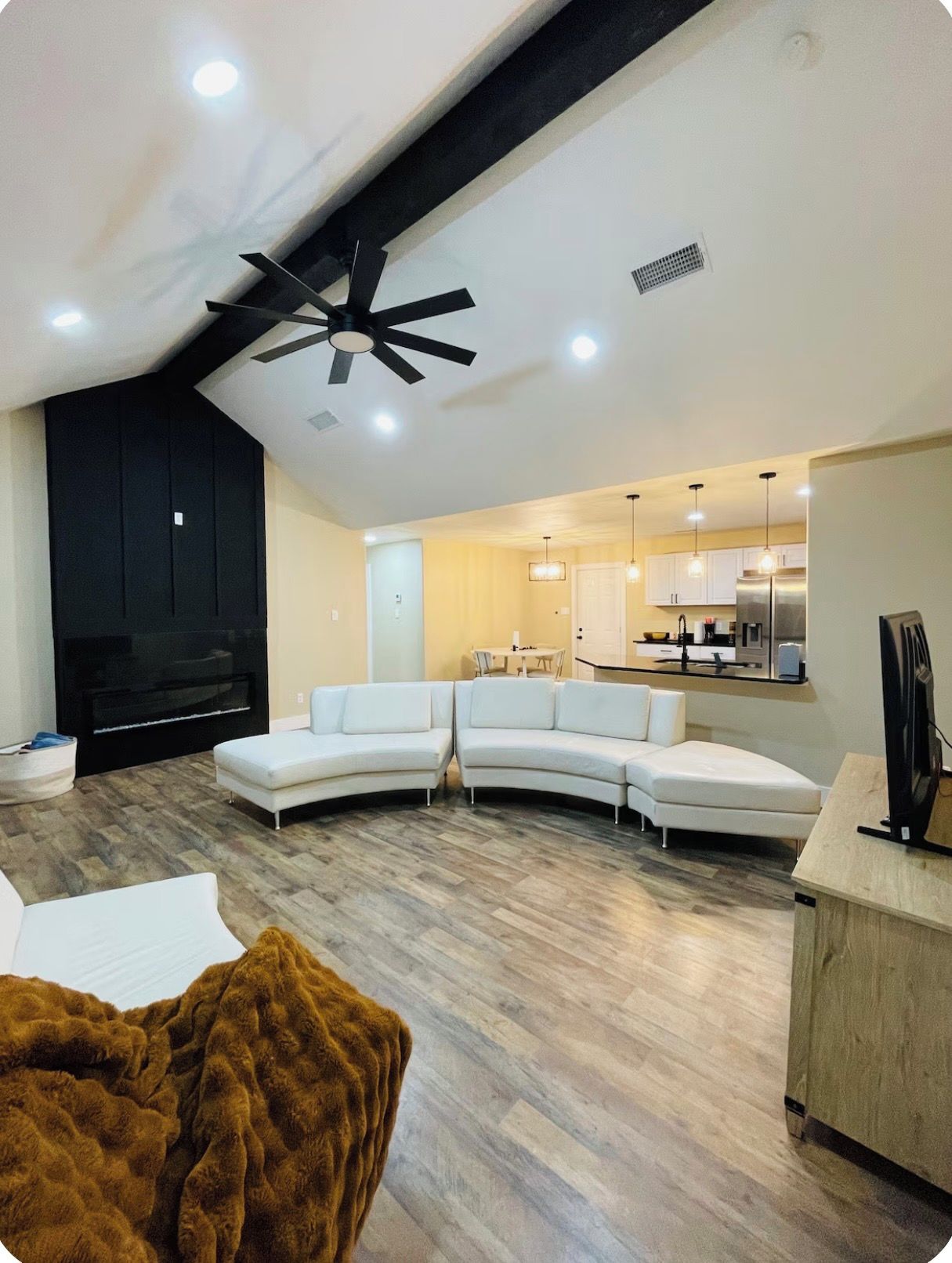A modern living room with a sectional sofa, a flat-screen TV, and a ceiling fan.
