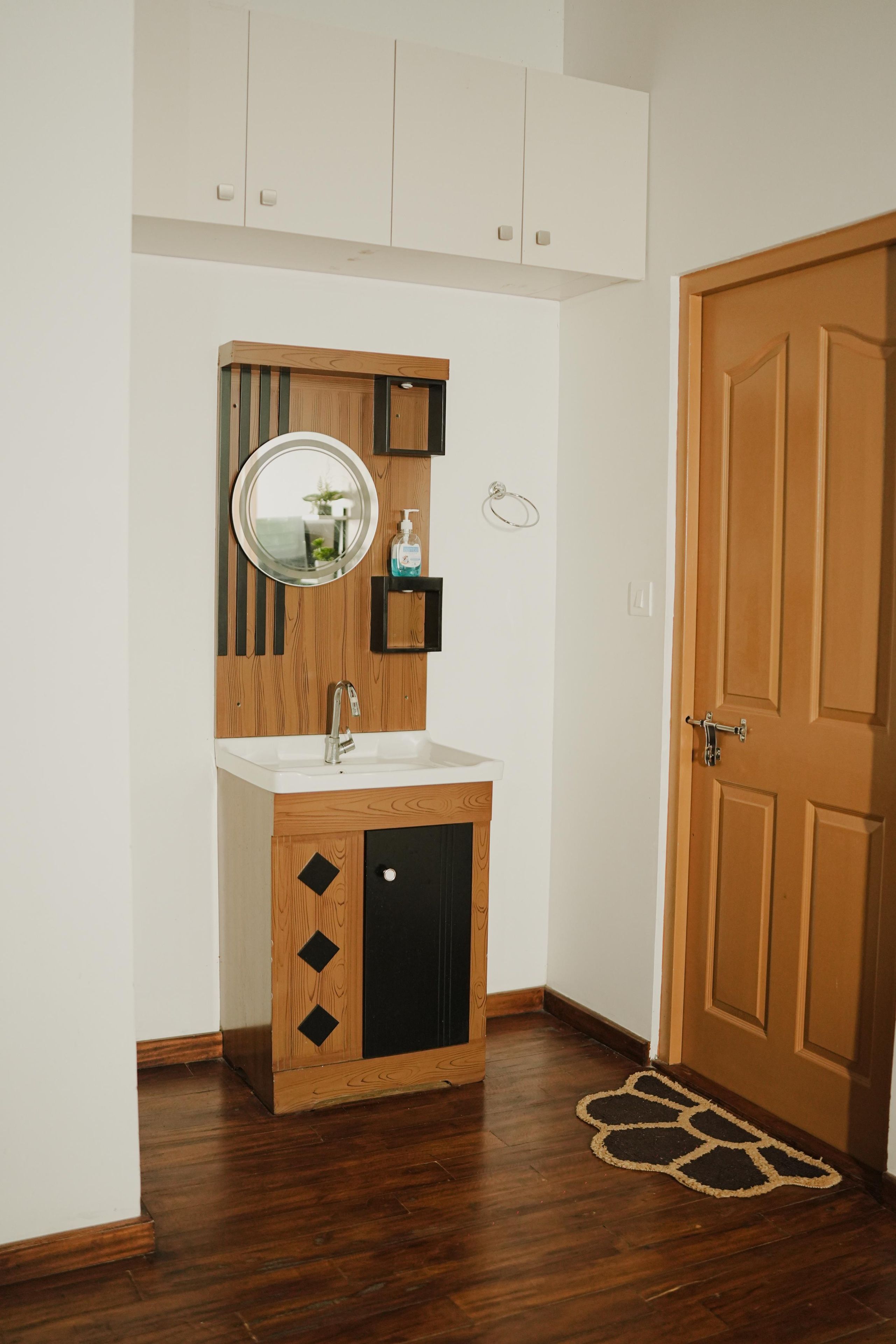 Un baño con tocador de madera, espejo redondo, lavamanos y una puerta.