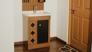 Un baño con tocador de madera, espejo redondo, lavamanos y una puerta.