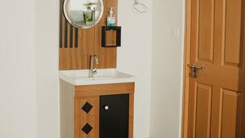 Un baño con tocador de madera, espejo redondo, lavamanos y una puerta.