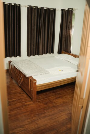 A single bed with a wooden frame and white bedding in a room with dark curtains.