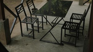 Un espacio de estar al aire libre cubierto, con mesa y sillas, rodeado de follaje.