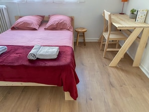 A room with a bed, a small wooden desk, a chair, a red blanket, and a rolled-up towel. - Hostcare - Le Fredet | L’instant grenoblois (Grenoble)