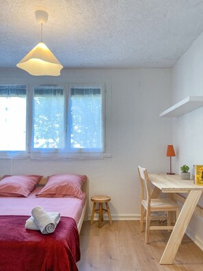 Een slaapkamer met een bed, een bureau, een stoel, een klein krukje en een hanglamp.