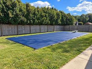 A backyard with a blue tarp laid out on the grass, a wooden fence, and a clear sky.