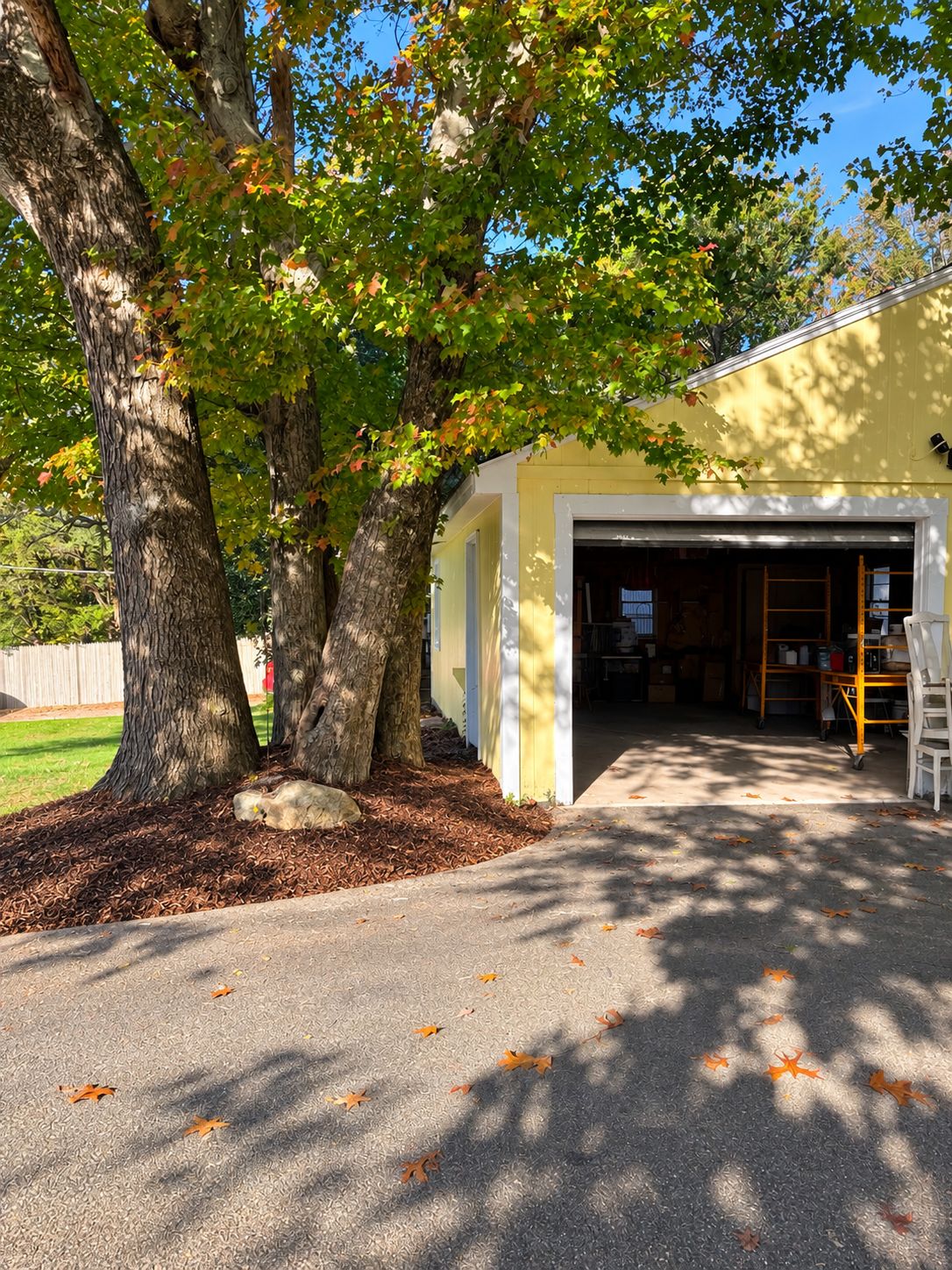 A garage with a yellow exterior, trees in the foreground, and a clear sky.