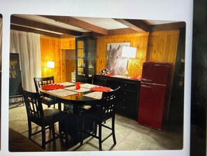 Uma área de refeições com mesa e cadeiras de madeira, uma geladeira vermelha e um armário com portas de vidro.