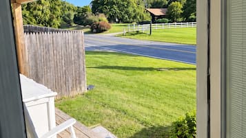 A wooden deck with a white chair, a view of a road, and a grassy area with trees.