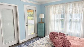 A bedroom with a bed, a dresser, a lamp, and a window with sheer curtains.