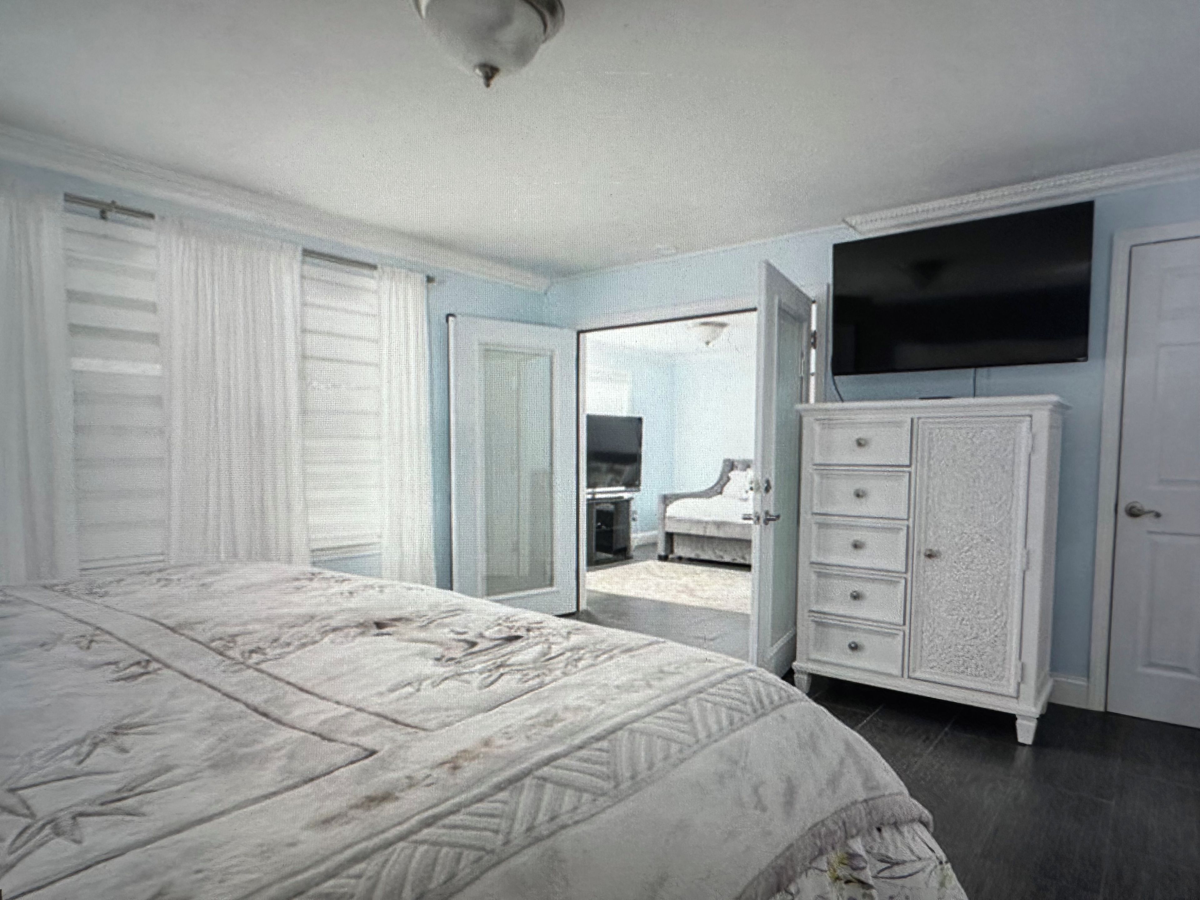 Une chambre à coucher comprenant un lit, une commode, un téléviseur et une porte donnant sur un balcon.