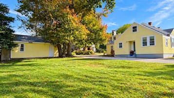 Una zona residencial con dos casas, un césped bien cuidado y un gran árbol de follaje otoñal.