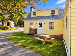 A yellow house with a stone chimney, a wooden door, and a picnic table in the front yard.