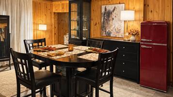 A dining area with a wooden table set for four, surrounded by chairs, and a red refrigerator to the right.