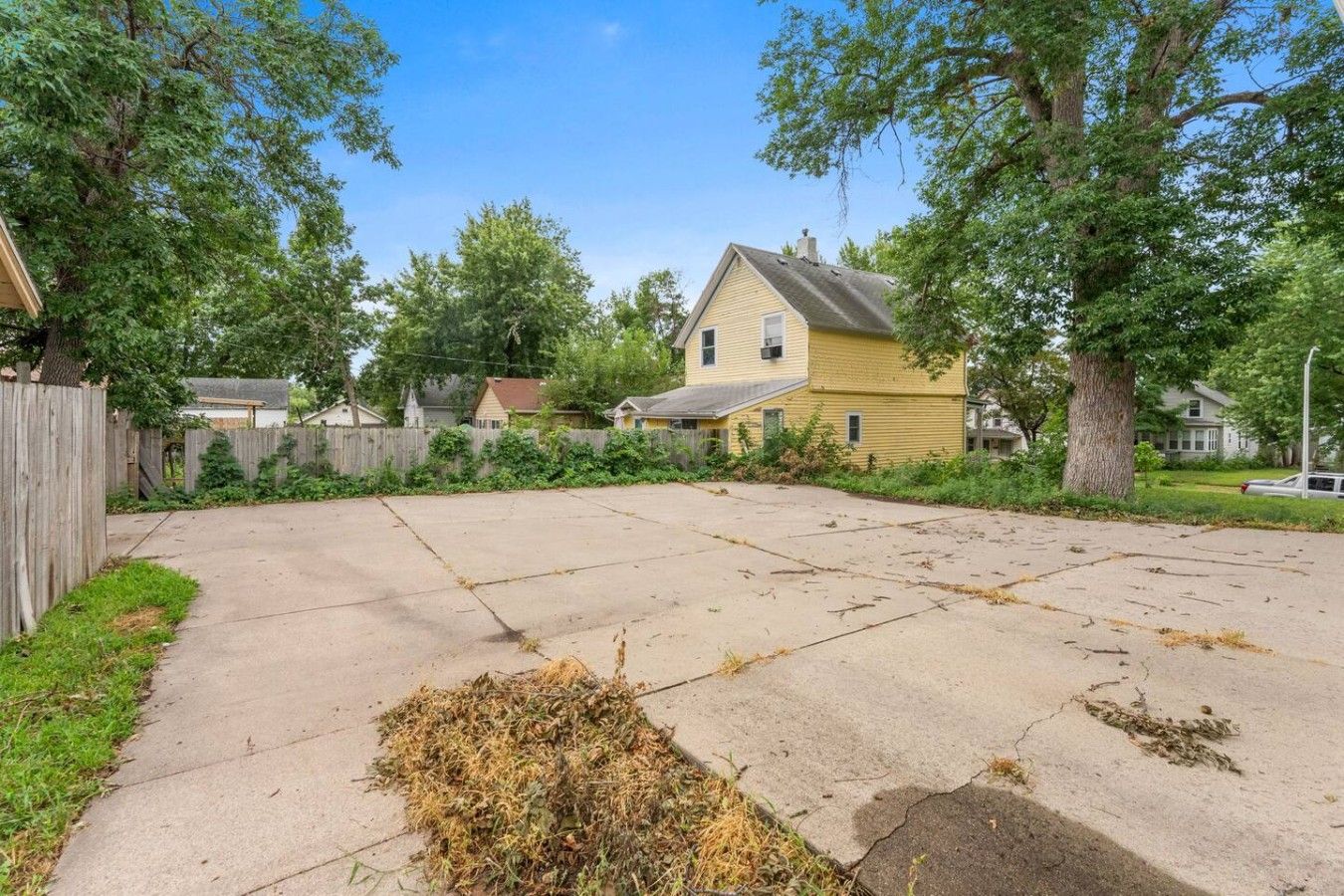 A residential backyard with a concrete patio, a wooden fence, and a yellow house.