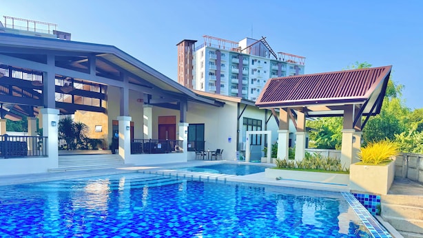 Una piscina con zona de solárium con baldosas, área de estar techada y vista a un edificio de varios pisos al fondo.