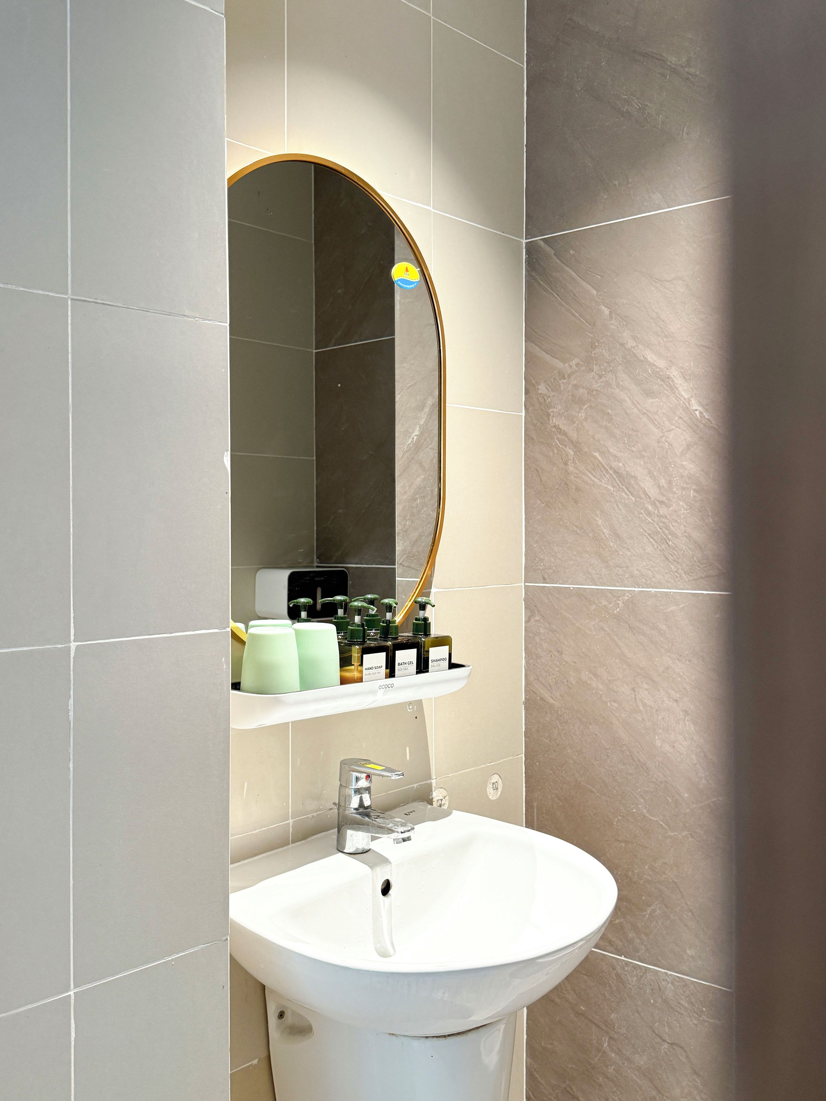 A bathroom with a white sink, a mirror with a gold frame, and a shelf with toiletries.
