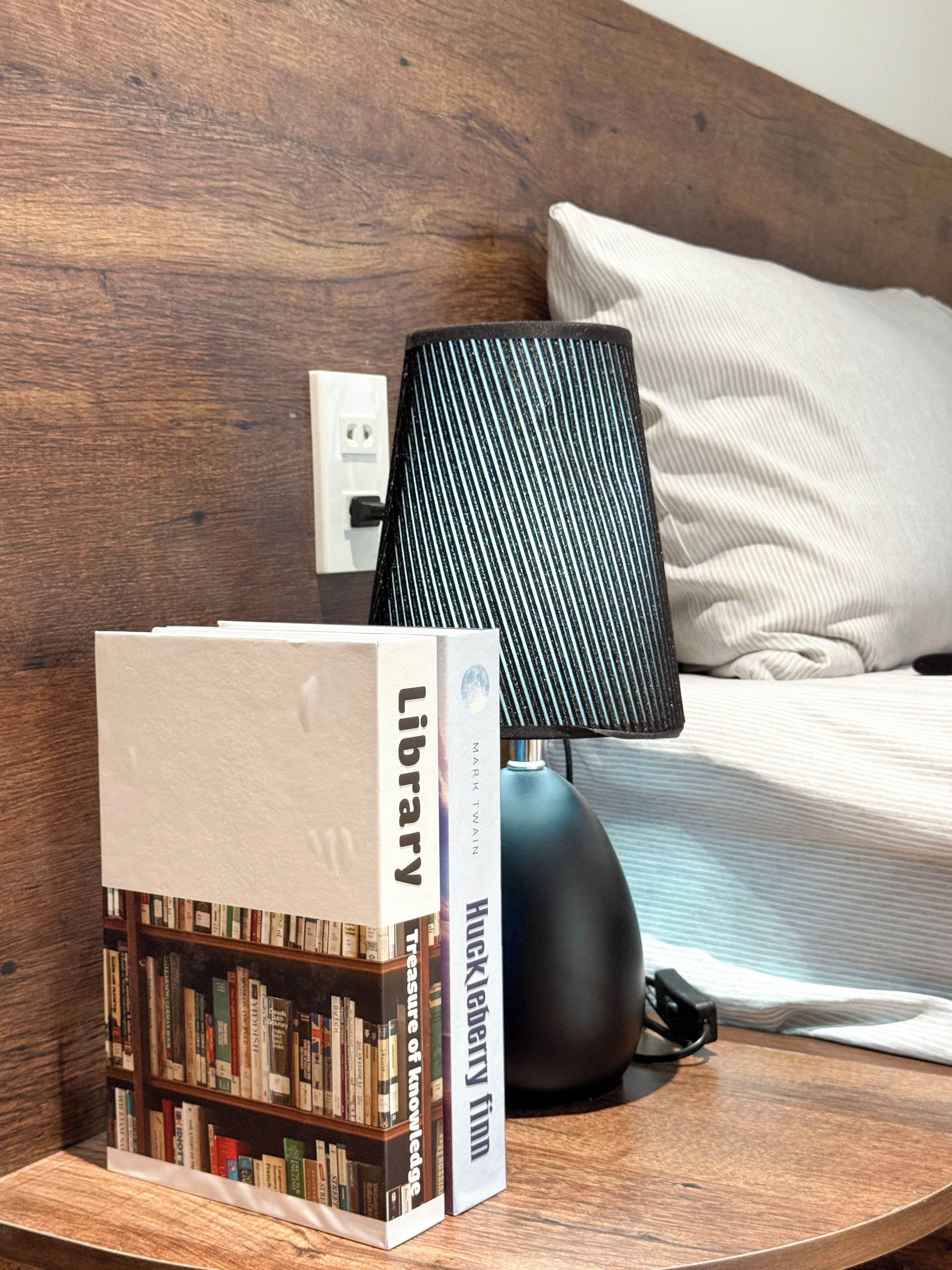 A bookshelf with books, a lamp, and a bed in a room with wooden walls.