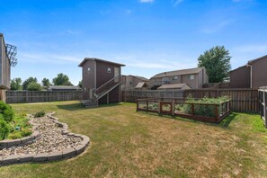 A residential backyard with a wooden deck, a raised garden bed, and a staircase leading to a building.