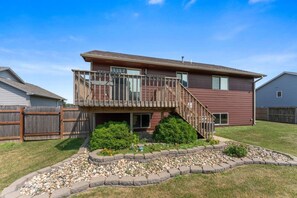 A two-story house with a wooden deck and a stone pathway leading to the front door.