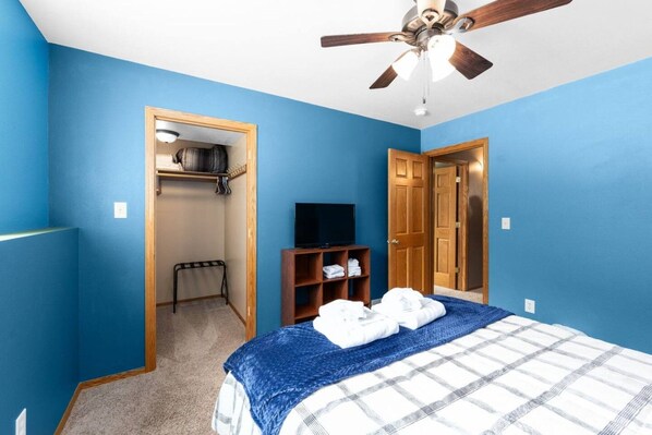 A bedroom with a bed, a ceiling fan, a television, a wardrobe, and a closet.