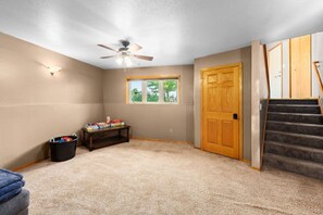 A carpeted room with a ceiling fan, a wooden door, and a window with a view of trees.