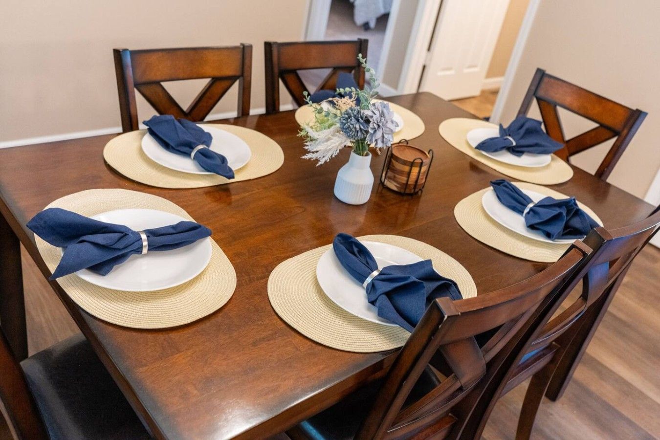 Een eettafel gedekt voor zes personen, met tafelmatten, borden en gevouwen servetten.