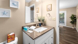Een badkamer met een grote spiegel, een wastafel en een toilet. Er hangen ingelijste foto's aan de muur en er staat een plant in de hoek.