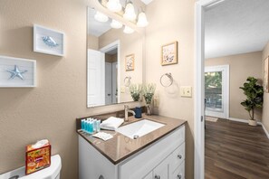 A bathroom with a large mirror, a sink, and a toilet. There are framed pictures on the wall and a plant in the corner. - Pioneer Place | King Bed | Deck | 3-Min to Avera (Sioux Falls)