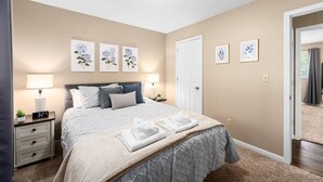 Een slaapkamer met een bed, nachtlampen, een nachtkastje, een deur en wanddecoratie.